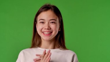 Çocuk duyguları konsepti. Mutlu yüzlü Asyalı bir kız çocuğu kameraya ve alkışlayan ellere bakar, olumlu ifade, krom anahtar yeşil ekran arka plan modelinde izole edilmiş.