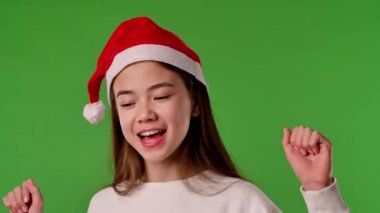 Çocuk duyguları konsepti. Noel Baba şapkalı Asyalı kız kameraya şarkı söylüyor, pozitif ifade, yeşil ekran arka plan modelinde izole edilmiş..