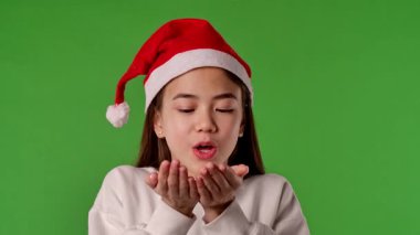 Çocuk duyguları konsepti. Noel Baba şapkalı Asyalı kız çocuğu elleri karları uçuruyor ve etrafına bakıyor, pozitif ifade, krom anahtar yeşil ekranda izole edilmiş arka plan modeli..