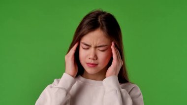 Çocuk duyguları konsepti. Asyalı kızın başı ağrıyor, baş ve masaj tapınakları var, acı dolu bir ifade, krom anahtar yeşil ekran stüdyo arka planında izole edilmiş..