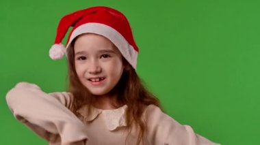Çocuk duyguları konsepti. Noel Baba şapkalı küçük kız kamerada şarkı söylüyor, pozitif ifade, yeşil ekranda izole edilmiş arka plan modeli..