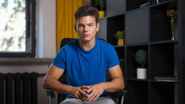 Çevrimiçi kursa katılan kişi. Üniversitede okuyan erkek öğrenci, sandalyede oturuyor, internette ders dinliyor, öğretmenini selamlıyor, el sallıyor. Modern online eğitim.