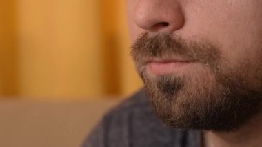 Genç adam evde vakit geçiriyor. Yetişkin sakallı adam yakından çekim yapıyor, erkek patates cipsi yiyor, abur cubur çiğniyor, abur cuburdan hoşlanıyor. Boş zaman ve günlük yaşam konsepti.