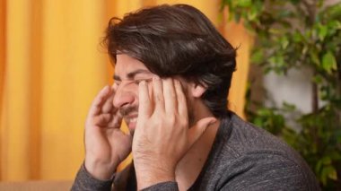 İnsani duygular ve ifadeler kavramı. Yetişkin bir adam kanepeye yakın oturuyor. Başı ağrıyor. Yüzünde acı ifadesi var. Kameraya poz veren erkek model..