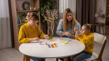 Mutlu aile tatile hazırlanıyor. Anne ve küçük kızlar Paskalya kutlamalarına hazırlanıyor, masada oturmuş geleneksel bahar buketini süslüyor, kurdele ve yumurta takıyorlar..