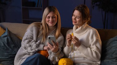 Geleneksel zanaat ve hobiler. İki bayan arkadaş geceyi hobi olarak evde el işi yaparak, kanepede oturup iplik ve iğneler kullanarak örgü örerek, akıllı telefondaki selfie resimlerine bakarak geçiriyorlar..