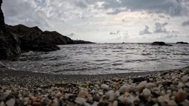 İspanya 'da kayalık bir kıyı şeridine yakın, berrak su kayaların üzerinden Akdeniz' e doğru yavaşça akıyor. Karanlık, ıslak kayalar yumuşak gökyüzü ile tezat oluşturarak sakin bir kıyı manzarası yaratıyor..