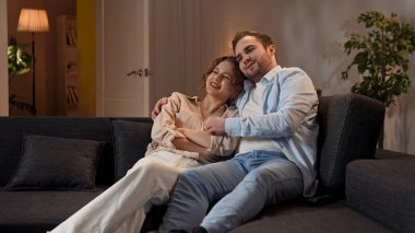 Mutlu çift birlikte vakit geçiriyor. Hoş bir çift evdeki kanepede dinleniyor, kadın ve erkek televizyon seyrediyor, sarılıyorlar, mutlu bir yüz ifadesi var..