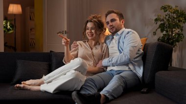 Mutlu çift birlikte vakit geçiriyor. Hoş bir çift evdeki kanepede dinleniyor, kadın ve erkek televizyon seyrediyor, sarılıyorlar, mutlu bir yüz ifadesi var..