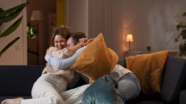 Mutlu çift birlikte vakit geçiriyor. Evdeki kanepede dinlenen sevimli bir çift yastık savaşında oynayan bir kadın ve bir erkek şakalaşıyor ve sarılıyorlar..