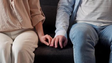 Mutlu çift birlikte vakit geçiriyor. Evdeki kanepede dinlenen sevimli bir çift, kadın ve erkeğin kanepede oturup el ele tutuşurken yakın çekimleri. Yavaş çekim.