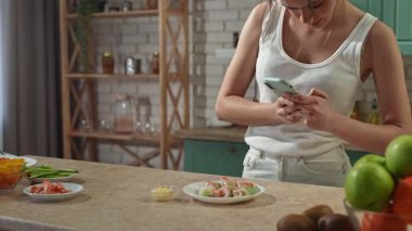 Sağlıklı beslenme konsepti. Mutfaktaki masada genç bir kadın sağlıklı öğle yemeği için börek hazırlıyor. Akıllı telefonuyla taze böreklerle ve selfielerle fotoğraf çekiyor. Yavaş çekim.