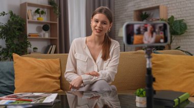 Sıcak bir kayıt stüdyosunda, bir kadın tutkuyla konuşur ve akıllı telefonuyla bir video blogu kaydeder, podcast 'in özünü aktarır. Atmosfer parlak, yeşillik ve modern dekorla.