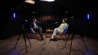 Şık bir stüdyoda, etkili bir stüdyoda ve podcast sunucu değişim anlayışında. Profesyonel ışıklandırma ve kayıt cihazlarıyla çevrili iki mikrofon derin tartışmalarını kaydediyor. Sahne arkasında