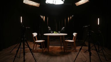 Modern bir stüdyoda, yumuşak ışıklandırmayla çevrili ahşap bir masada hazır bekleyen iki mikrofon. Sahne arkasında