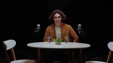Minimalist bir stüdyoda dairesel bir masada oturan nüfuzlu biri, podcast röportajına hazırlanıyor..