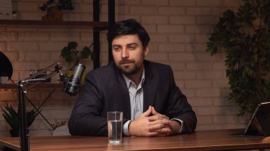 Çağdaş bir podcast stüdyosunda, iyi giyimli bir birey ahşap bir masada oturup düşünceli bir sohbete dalıyor..