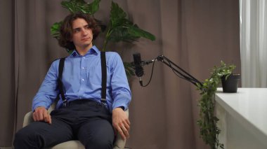 Modern bir podcast stüdyosunda, bir uzman etkili bir röportaj için hazırlanır, mikrofon her kelimeyi kaydederken rahat bir şekilde, yemyeşil dekorun ortasında..