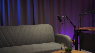 Rahat bir podcast stüdyosu heyecan verici bir röportaj için hazır. İç açıcı konuşmaları yakalamak için hazırlanmış bir mikrofonu sergiliyor. Sakinleştirici renklerle ve rahatlatıcı bir atmosferle çevrili..