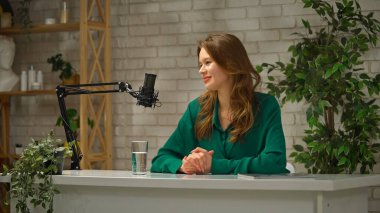 Uzman bir hikaye anlatıcısı şık bir podcast stüdyosunda oturmuş, ilginç bir röportaj kaydedilirken sezgilerini paylaşıyor. Doğal elementler ve minimalist dekor yaratıcı atmosferi geliştirir..