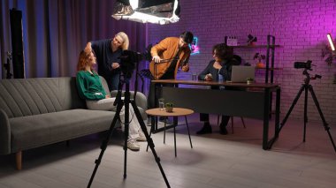 Sahne arkasında. Canlı bir podcast röportajı renkli bir stüdyoda yayınlanıyor. Etkilenenler hikaye anlatma tekniklerini tartışırken, bir ekip dinleyiciler için kusursuz bir kayıt deneyimi sağlayarak kurulumu hazırlıyor.