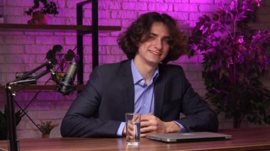 Genç bir erkek sunucu canlı bir stüdyo ortamında röportaj veya uzman videosu çeker. Podcast 'ini profesyonel bir mikrofon ve stüdyo ile kaydederek en son konulardaki düşüncelerini paylaşıyor.