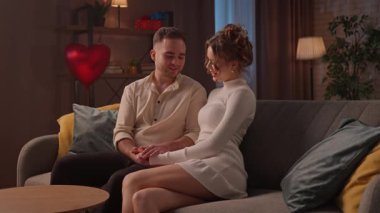 Sevgililer Günü 'nde evde birlikte olan sevimli bir çift. Sevgililer Günü 'nü evde kutlayan mutlu bir çift, kanepede oturup sarılıyorlar, kadın ve erkek konuşuyor ve el ele tutuşuyorlar. Yavaş çekim.