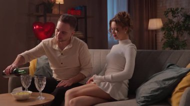 Sevgililer Günü 'nde evde birlikte olan sevimli bir çift. Sevgililer Günü 'nü evde, kanepede kutlayan mutlu bir çift. Adam bardaklara şarap doldurup kadına veriyor. Yavaş çekim.