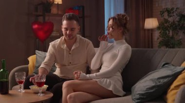 Sevgililer gününde evde hoş bir çift var. Sevgililer Günü 'nü evde, kanepede şarap içerek kutlayan mutlu bir çift. Kadın ve erkek konuşur ve birbirlerini üzümle beslerler. Yavaş çekim.
