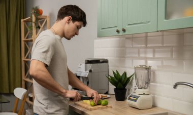 Günlük rutin yaşam tarzı konsepti. Sabahları mutfakta sağlıklı bir kahvaltı hazırlayan taze meyve püresi hazırlayan, kivi kesen genç bir adam..