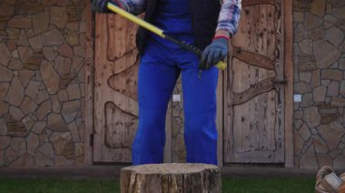 Kışın güneşli bir günde kalın giysiler içinde odun kıran genç bir adam. Bir adam baltayla odun kesiyor, kış için odun hazırlıyor..