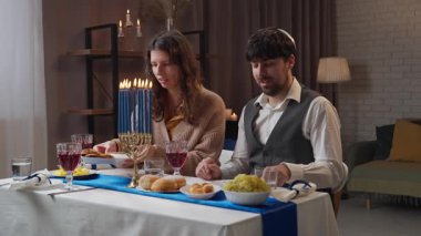 Aile tatil için hazırlanıyor. Geleneksel Hanuka kutlamalarına hazırlanan Yahudi çift, masada oturan erkek ve kadın, akşam yemeğinin ve sohbetin tadını çıkarıyorlar. Yavaş çekim.
