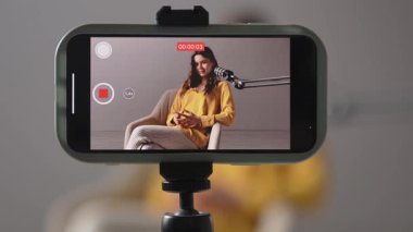 Sıcak bir kayıt stüdyosunda, bir kadın tutkuyla konuşur ve akıllı telefonuyla bir video blogu kaydeder. Bir kadın blogcu video blogunu kaydeder veya abonelerine canlı olarak yayınlar.