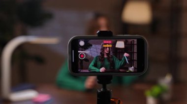 Sıcak bir kayıt stüdyosunda, bir kadın tutkuyla konuşur ve akıllı telefonuyla bir video blogu kaydeder. Bir kadın blogcu video blogunu kaydeder veya abonelerine canlı olarak yayınlar.