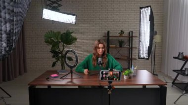 Uzman bir videonun sahne arkası kaydı. Sıcak bir kayıt stüdyosunda, bir kadın tutkuyla konuşur ve bir video blogu kaydeder. Bir kadın blogcu, abonelerine canlı yayın veya medya içeriğini kaydeder.