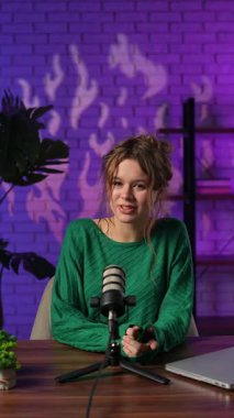 Stüdyoda rahat bir kadın, uzman videosu çekerken tutkuyla fikirleri tartışıyor. Yeşil kazaklı blogcu kadın markalaşma ve iş geliştirme stratejisinden bahsediyor. Dikey video.