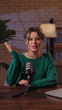 Stüdyoda rahat bir kadın, uzman videosu çekerken tutkuyla fikirleri tartışıyor. Yeşil kazaklı blogcu kadın markalaşma ve iş geliştirme stratejisinden bahsediyor. Dikey video.