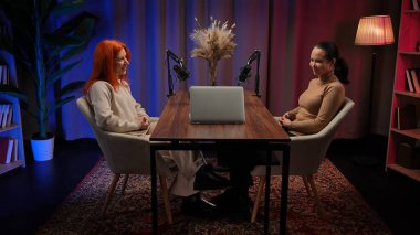 Modern bir tavan arası stüdyosunda podcastlar için röportaj yapan iki genç kadın etkili. Uzmanlar deneyimlerini paylaşıyor ve bir dizüstü bilgisayar kullanarak abonelerle iletişim kuruyorlar. İçerik materyali, video günlüğü.