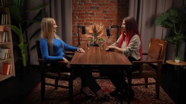 Modern bir tavan arası stüdyosunda podcastlar için röportaj yapan iki genç kadın etkili. Uzmanlar kayıt için stüdyo mikrofonlarını kullanarak deneyimlerini ve iletişimlerini paylaşıyorlar. İçerik materyali, video günlüğü.