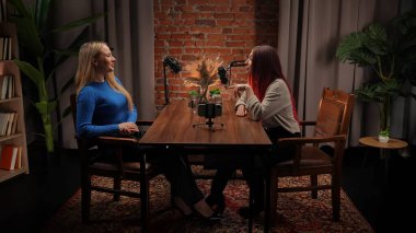 Modern bir tavan arası stüdyosunda podcastlar için röportaj yapan iki genç kadın etkili. Uzmanlar kayıt için stüdyo mikrofonlarını kullanarak deneyimlerini ve iletişimlerini paylaşıyorlar. Akıllı telefon kaydı.