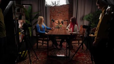 Sahne arkasında. Modern bir tavan arası stüdyosunda podcastlar için röportaj yapan iki genç kadın etkili. Espertler kayıt için stüdyo mikrofonlarını kullanarak deneyimlerini ve iletişimlerini paylaşırlar. İçerik malzemesi.