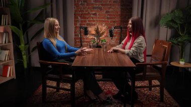 Modern bir tavan arası stüdyosunda podcastlar için röportaj yapan iki genç kadın etkili. Uzmanlar kayıt için stüdyo mikrofonlarını kullanarak deneyimlerini ve iletişimlerini paylaşıyorlar. İçerik materyali, video günlüğü.