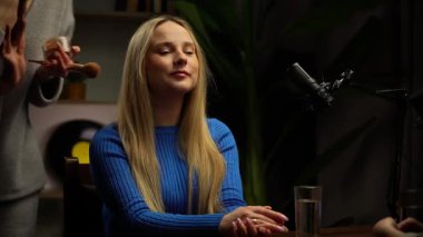 Sahne arkasında. Modern bir stüdyo stüdyosunda podcast için bir kadın röportaj hazırlıyor. Makyaj ustası makyajını düzeltir ve yüzüne pudra sürer. Video günlüğü, içerik kaydı.