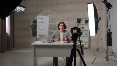 Sahne arkasında, parlak ve şık bir podcast stüdyosunda, içerik yaratıcısı güven içinde bir masada oturuyor, röportaj için hazır. Bir kamera değiş tokuşu kaydeder, yaratıcılık sürecini vurgular..