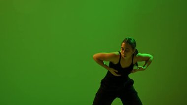 Siyah kıyafetli genç bir bayan dansçı, dramatik neon ışıkları altında yeşil renkler kullanarak dinamik ve sanatsal bir atmosfer yaratarak çağdaş dans figürü sergiliyor. Yavaş çekim