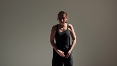 Siyah kıyafetli genç bir dansçı stüdyoda çarpıcı bir şekilde modern dans hareketleri sergiliyor. Kadın zarif bir şekilde dans ederek dinamik ve sanatsal bir atmosfer yaratıyor. Yavaş çekim