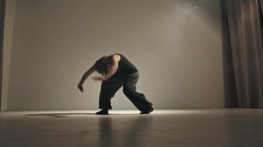 Siyah kıyafetli genç bir dansçı stüdyoda çarpıcı bir şekilde modern dans hareketleri sergiliyor. Kadın zarif bir şekilde dans ederek dinamik ve sanatsal bir atmosfer yaratıyor. Yavaş çekim
