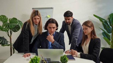 Çeşitli profesyonellerden oluşan bir grup, modern ofis ortamında bir dizüstü bilgisayardaki verileri ve notları olan bir beyaz tahtayı analiz ederek bir iş stratejisi üzerinde işbirliği yapıyor..