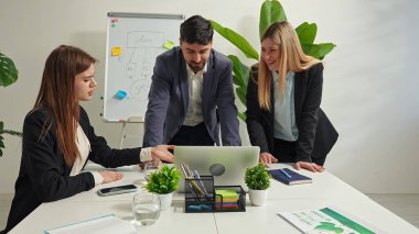 Çeşitli profesyonellerden oluşan bir grup, modern ofis ortamında bir dizüstü bilgisayardaki verileri ve notları olan bir beyaz tahtayı analiz ederek bir iş stratejisi üzerinde işbirliği yapıyor..