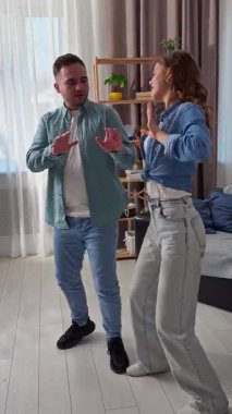 Hafta sonları birlikte birkaç boş zaman geçiririz. Çift evdeki kanepede dinleniyor, kadın ve erkek odada duruyor ve enerjik bir şekilde dans ediyor, gülümsüyor ve nazikçe dokunuyorlar. Dikey video.